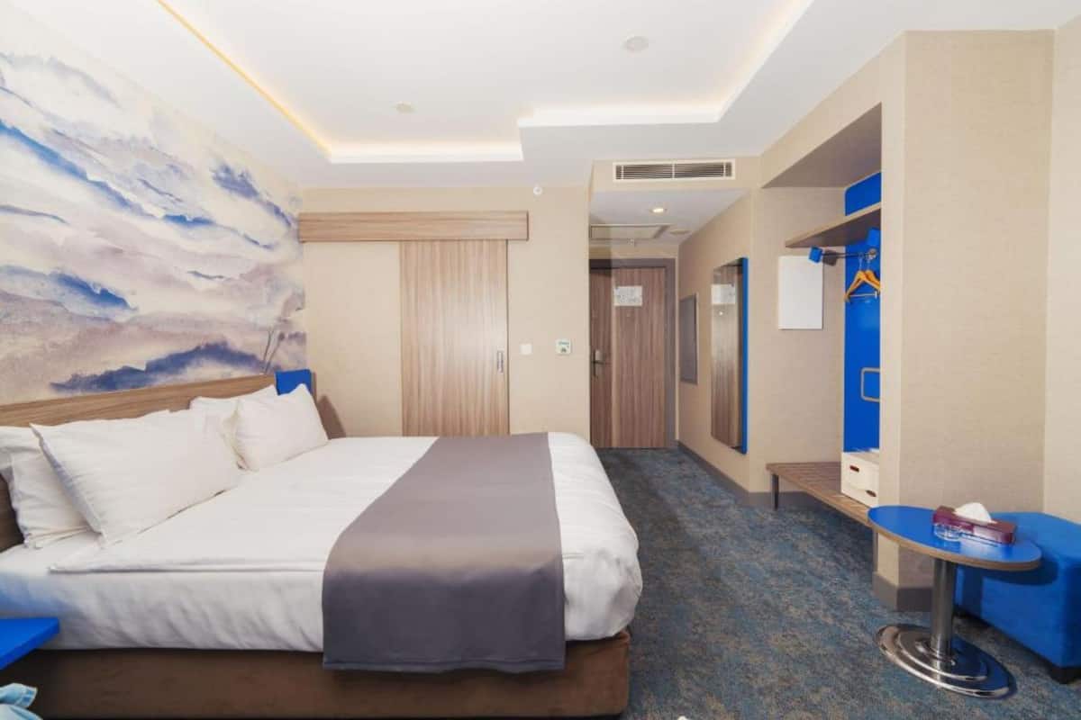 Habitación de hotel con una cama grande, una mesita pequeña, un espejo y un cuadro en la pared.