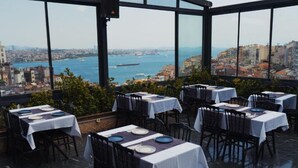En restaurang på taket med bord uppställda för middag, med utsikt över stadssiluetten och havet.