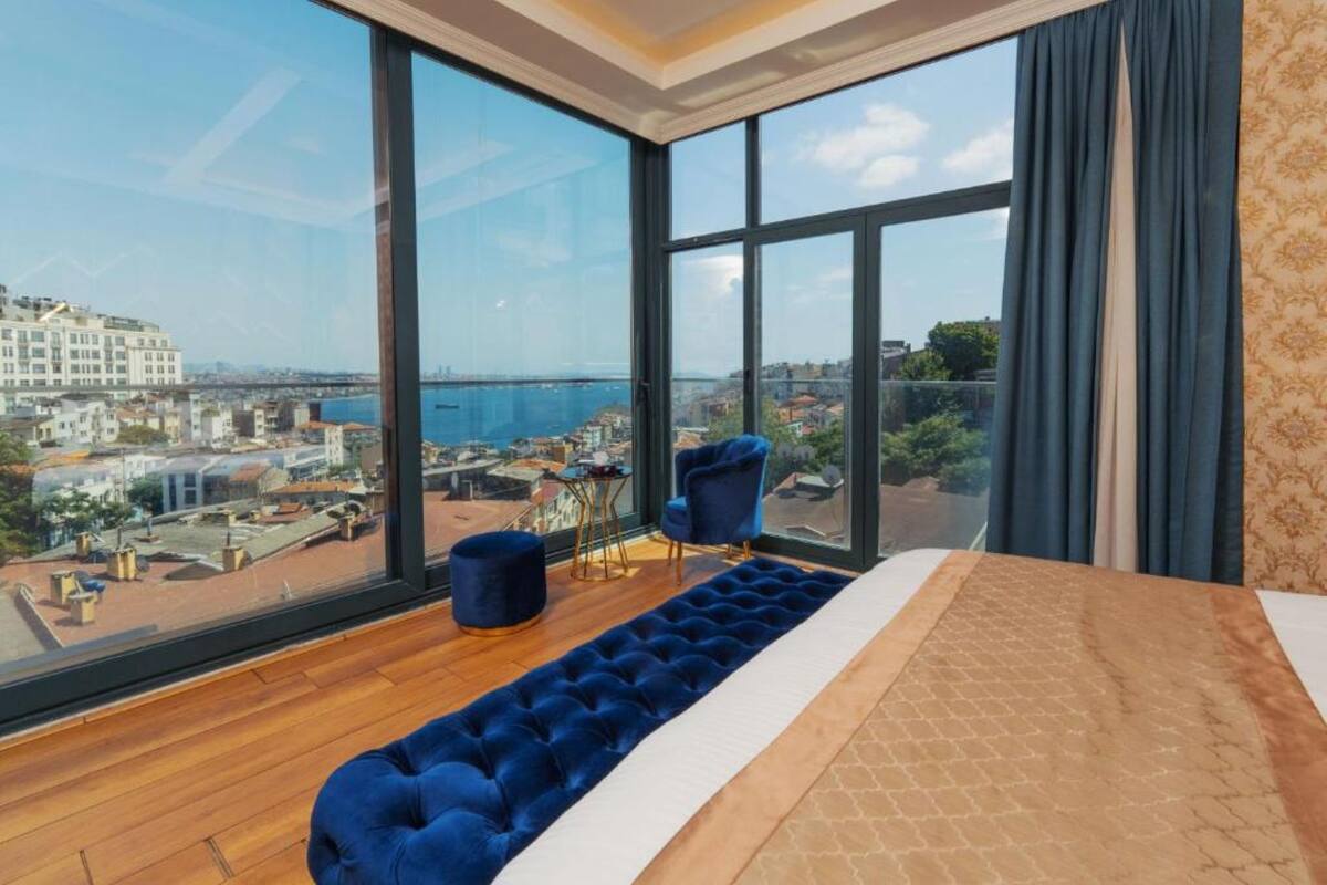Un dormitorio moderno con un ventanal grande, un sofá azul y vistas a un paisaje urbano.