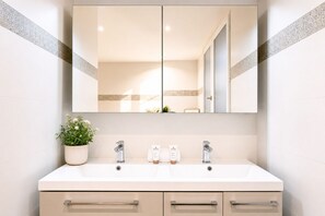 A bathroom with a double vanity, two sinks, a mirror, a potted plant, and toiletries. - 1597 Amelot (Paris)