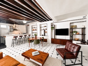 Una sala de estar moderna con una mesa de centro de madera, un sofá de cuero y un comedor con taburetes de bar.
