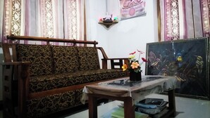 A living room with a patterned sofa, a small table with a vase of flowers, a framed picture on the wall, and a bookshelf with books.