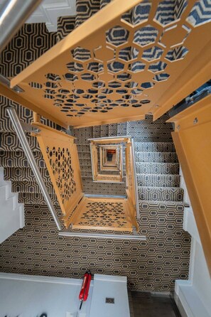 A spiral staircase with a geometric patterned wall and a wooden handrail.