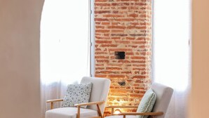 A cozy room with a brick wall, two white armchairs, a wooden table, and a patterned rug. - Gambetta Apartment – Right in the Heart of Gaillac (Gaillac)