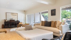 Een ruime woonkamer met een grote bank, een houten salontafel en een eethoek met een tafel en stoelen. Een groot raam biedt uitzicht op het omliggende landschap.