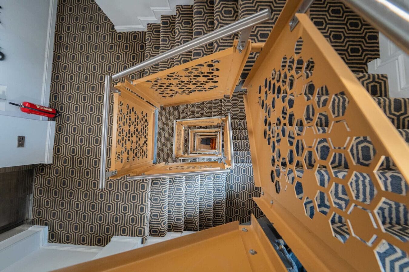 A spiral staircase with a geometric patterned wall and a red fire extinguisher on the left.