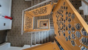 Un escalier en colimaçon, avec un mur orné d’un motif géométrique et un extincteur rouge placé sur le côté gauche.