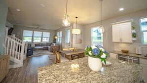 Eine geräumige Küche mit Granitarbeitsplatten, ein Essbereich mit Holztisch und ein Wohnzimmer mit Sofa und Treppe.