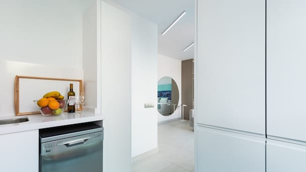 A modern kitchen with white cabinetry, a dishwasher, a fruit bowl with oranges and bananas, and a wine bottle. - Apartment in Las Palmas Near Las Canteras Beach (Las Palmas de Gran Canaria)