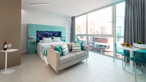A modern hotel room with a bed, a small table with a bottle and glass, a dining area with a table and chairs, and a large window with curtains. - Apartment in Las Palmas Near Las Canteras Beach (Las Palmas de Gran Canaria)