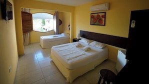 Una camera d'albergo con due letti, una finestra con tende, un quadro di fiori e un condizionatore d'aria.