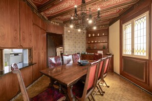 Un comedor con una mesa de madera, sillas, una araña y un papel tapiz estampado.