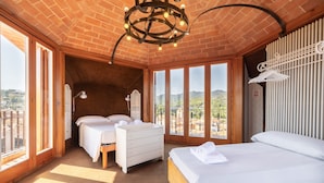 Ein Zimmer mit Backstein Decke, einem Bett, einem Schminktisch, einem Schreibtisch und großen Fenstern mit Blick ins Freie.