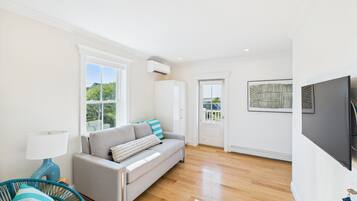 A modern living room with a grey sofa, a blue chair, a wooden floor, and a TV mounted on the wall.