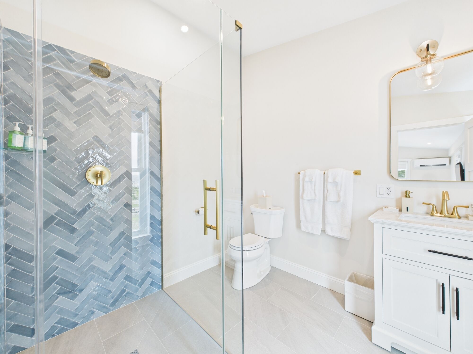 Un baño moderno con cabina de ducha de vidrio, inodoro blanco, tocador con grifo dorado y un espejo grande.