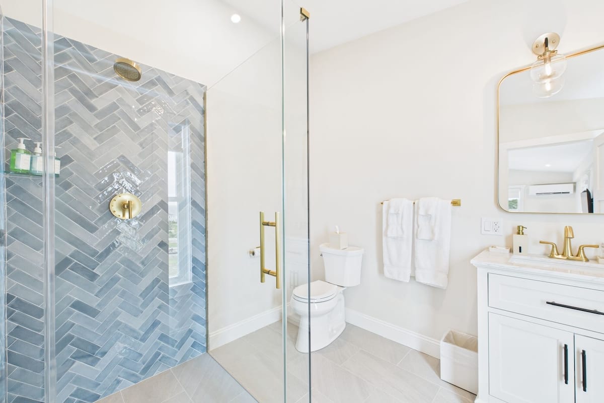 A modern bathroom with a glass shower enclosure, a white toilet, a vanity with a gold faucet, and a large mirror.