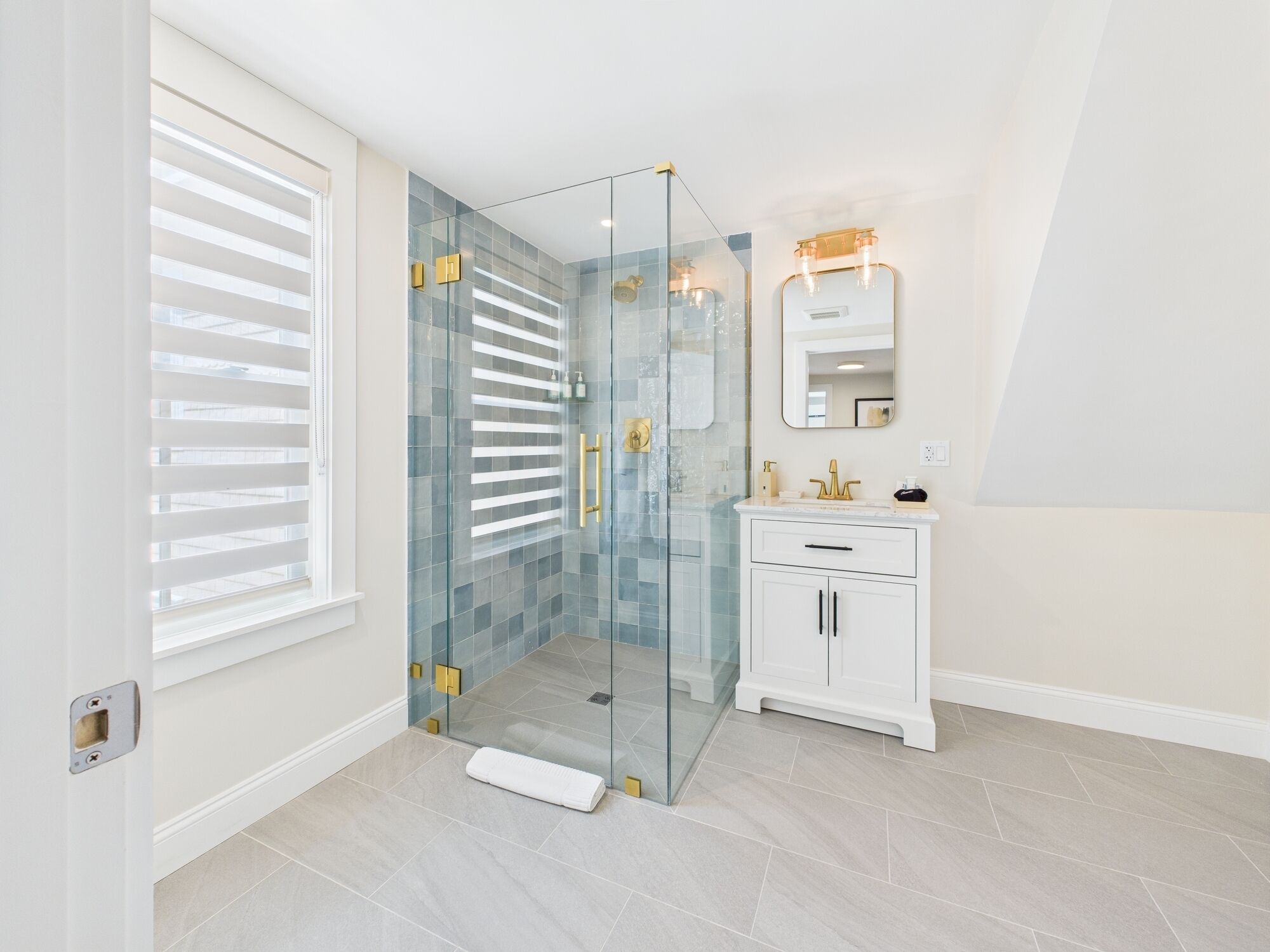 Een moderne badkamer met een douchecabine van glas, een wit wastafelmeubel met gouden details en een grote spiegel.