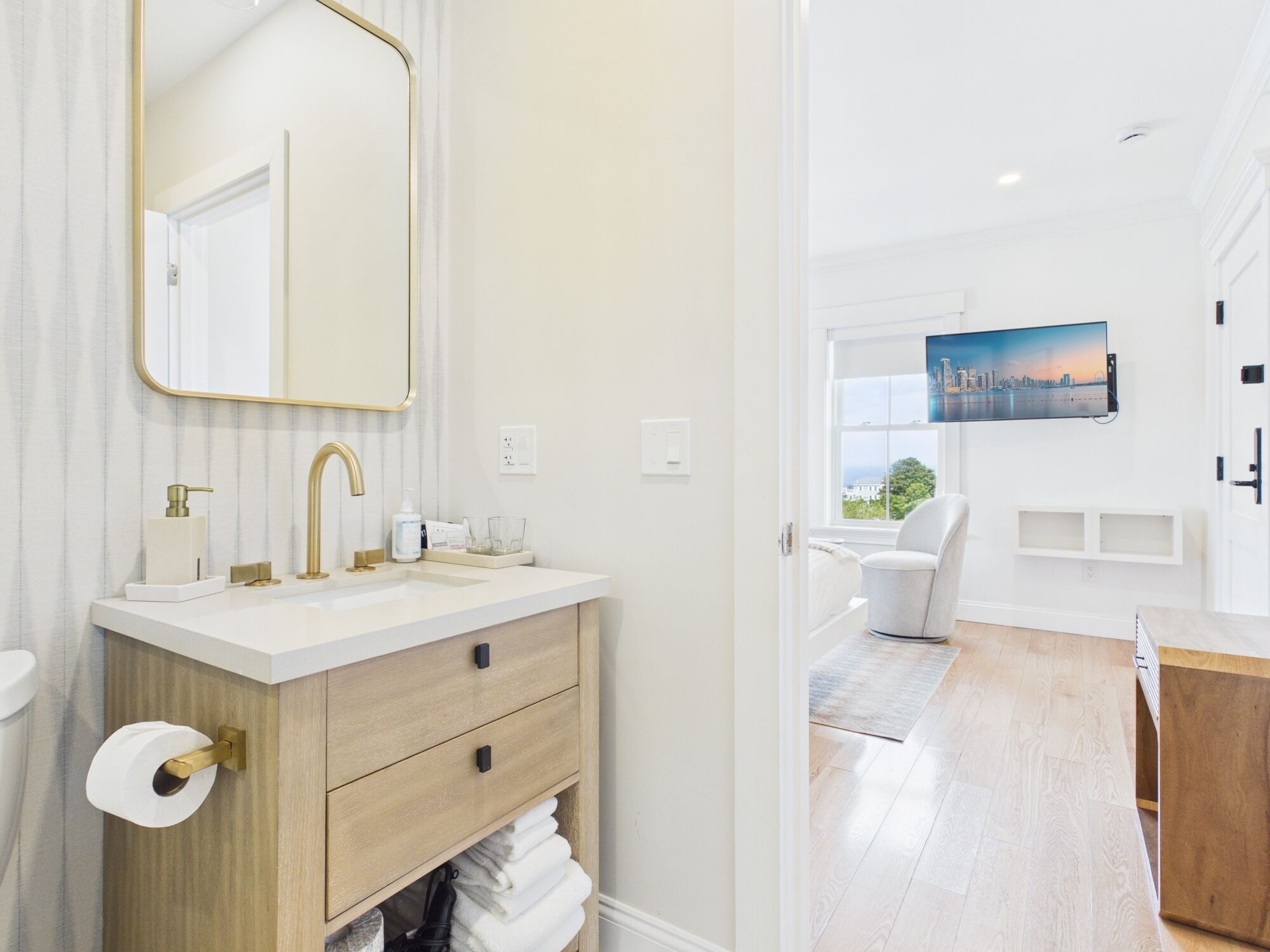 A modern bathroom with a white vanity, gold fixtures, and a large mirror.