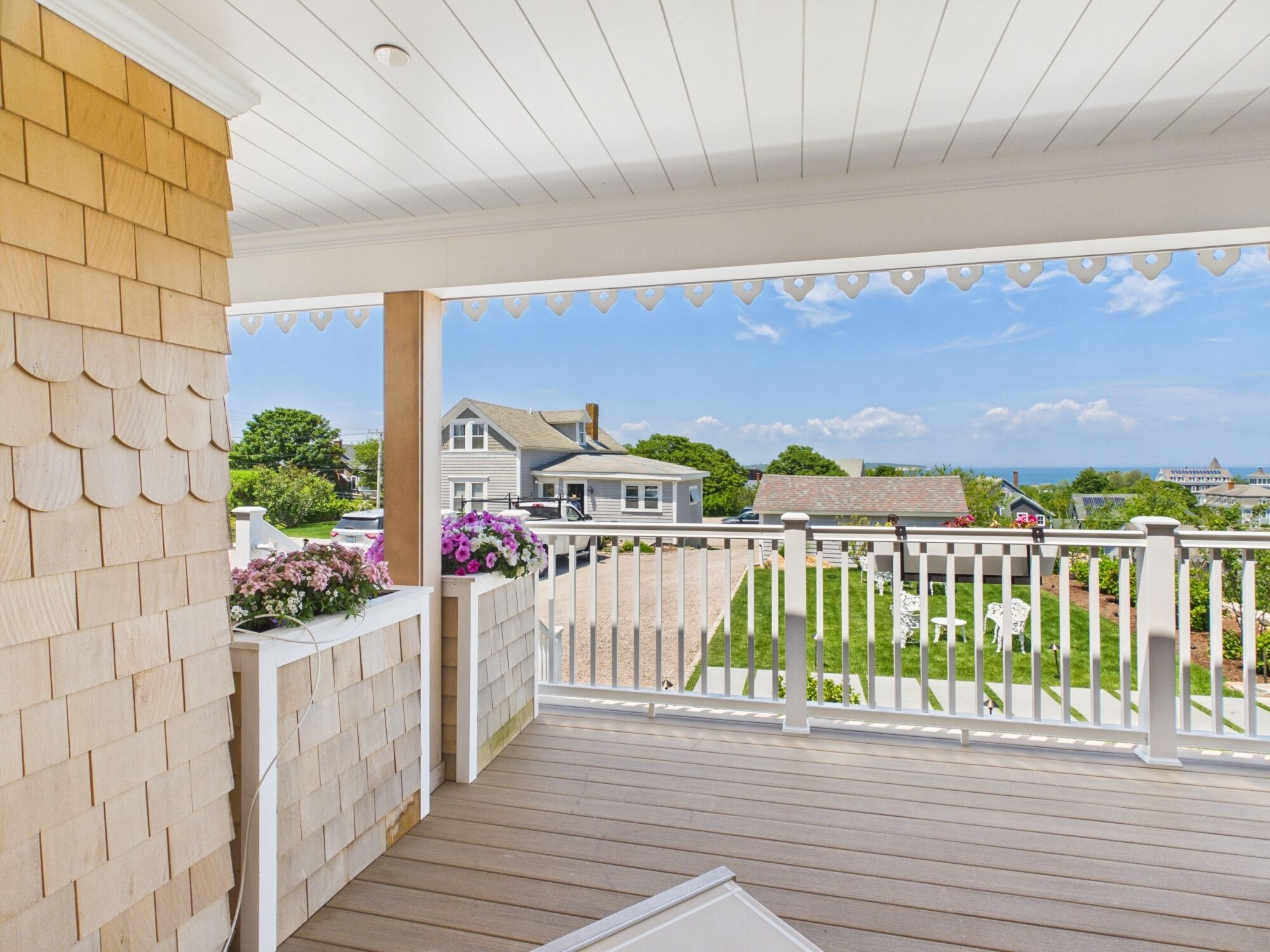 A wooden deck with a white railing, a brick wall, and a view of houses and greenery.