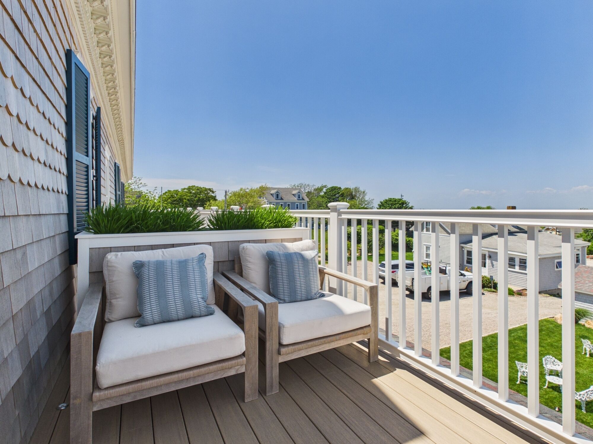 A balcony with two cushioned chairs, a white railing, and a view of a residential area.