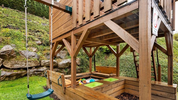 A wooden playhouse with a swing, a bench, and a small play area.