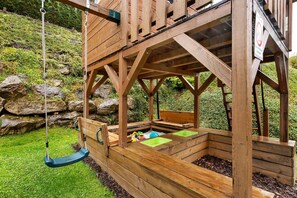 A wooden playhouse with a swing, a bench, and a small play area.