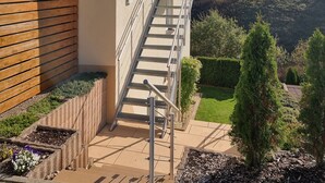 A building with a tiled roof, a staircase leading to a balcony, and a view of a green landscape.
