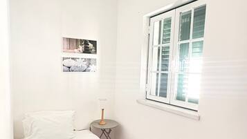 Une chambre à coucher avec un lit, une fenêtre, un tableau accroché au mur et une table de chevet avec une lampe.