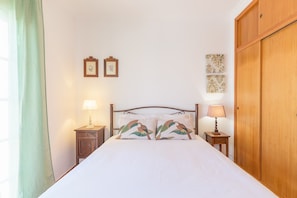 Un dormitorio con una cama, dos mesitas de noche con lámparas, un armario de madera y adornos en la pared.