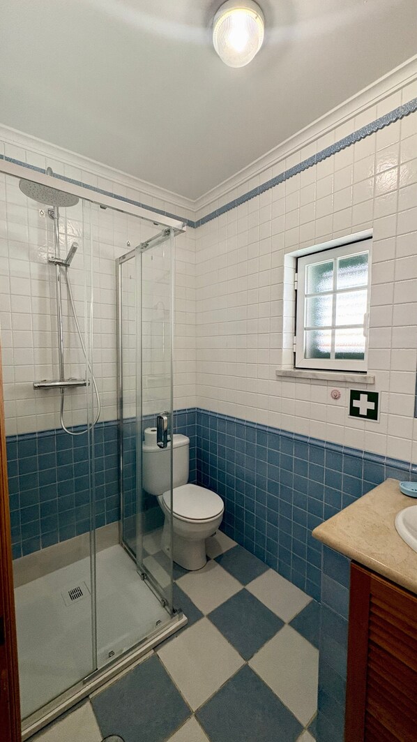 A bathroom with a glass shower enclosure, a toilet, and a sink.