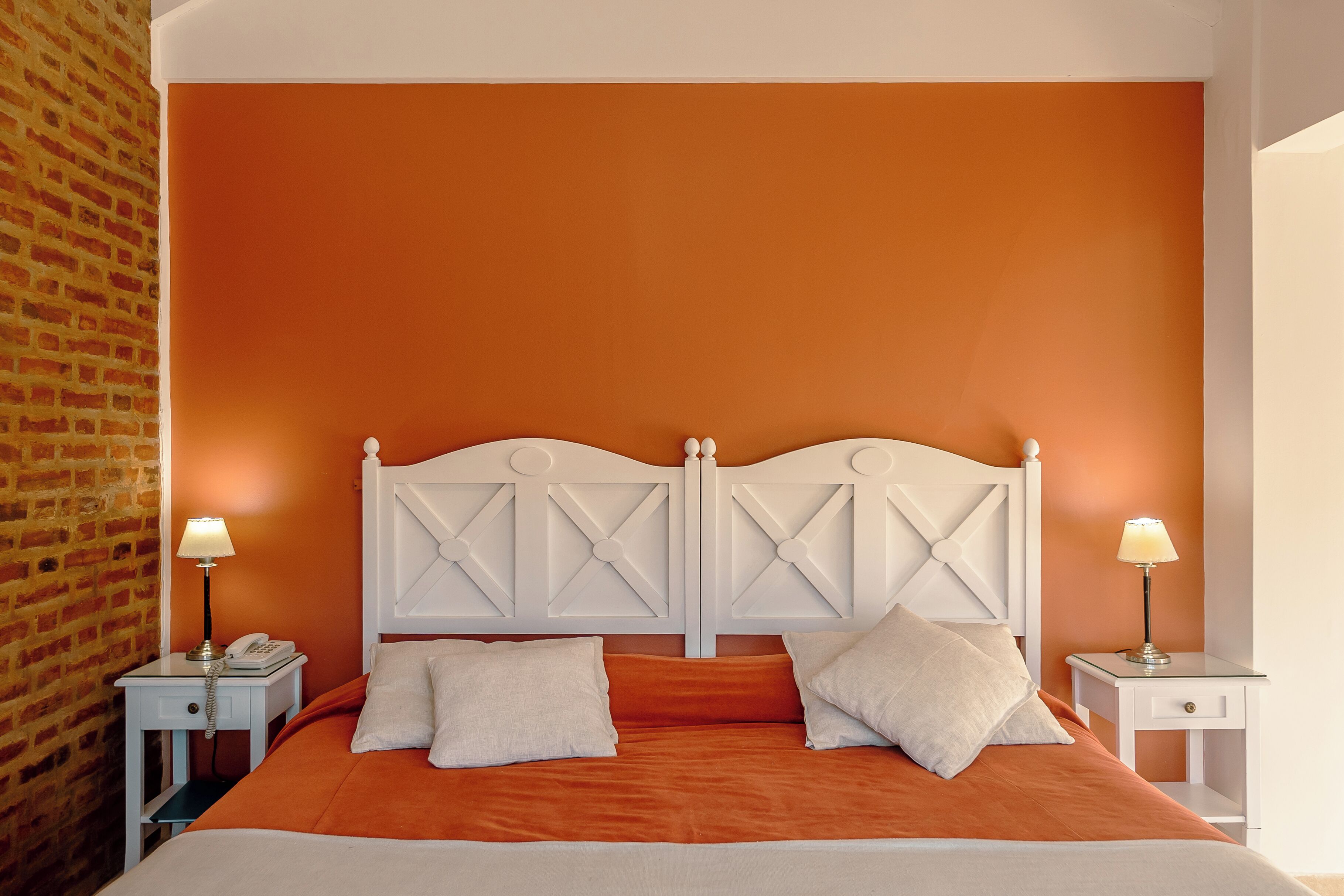 Una cama con colcha naranja, cabecera blanca y dos lámparas de noche.