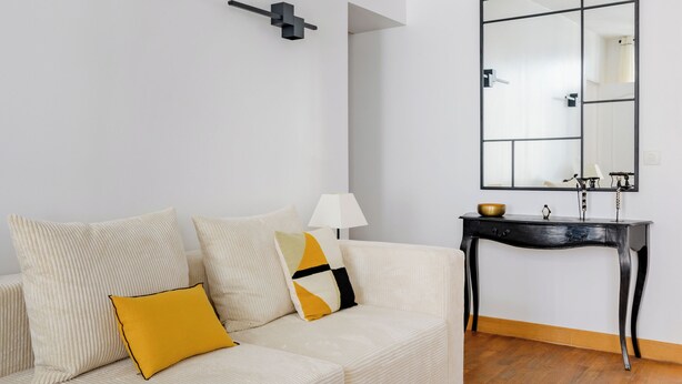 Un salon moderne avec un canapé blanc, des coussins jaunes, une console noire et un grand miroir.