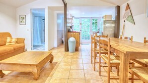 A spacious living area with a wooden dining table, sofa, and a view of the kitchen and outside.