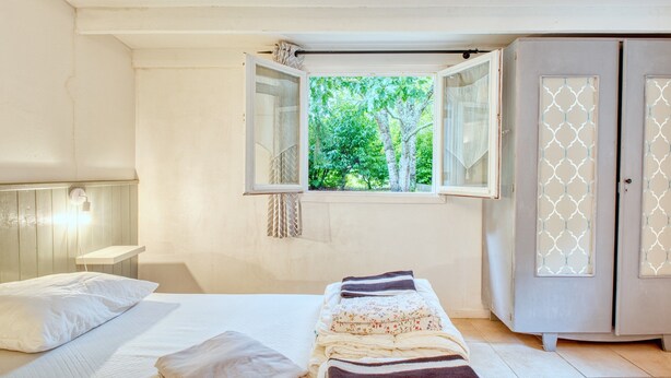 A bedroom with a bed, a window with an open view, a wardrobe, and a bedside lamp.