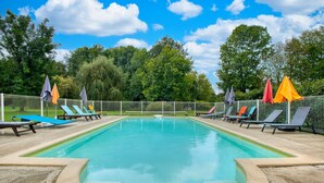 A rectangular swimming pool with a tiled deck, surrounded by a metal fence.
