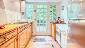 A kitchen with wooden cabinets, a sink, a stove, and a window with a view of greenery.