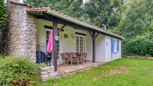 A stone building with a covered patio, a table with chairs, and a small garden area. - Gîte La Cascade - Domaine l'Étang des Mirandes with Shared Pool (Varaignes)