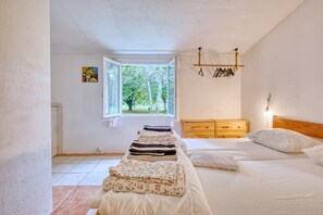 A bedroom with a bed, a wooden nightstand, a window with a view of trees, and a hanging light fixture. - Gîte La Cascade - Domaine l'Étang des Mirandes with Shared Pool (Varaignes)
