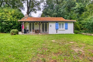 A small house with a tiled roof, a porch with a table and chairs, and a grassy yard. - Gîte La Cascade - Domaine l'Étang des Mirandes with Shared Pool (Varaignes)