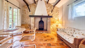 A cozy room with a stone wall, a fireplace, wicker furniture, and a dining table. - Gîte La Cascade - Domaine l'Étang des Mirandes with Shared Pool (Varaignes)