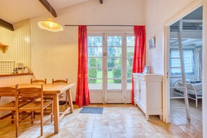 A room with a wooden dining table, chairs, a white cabinet, a ladder, and a window with red curtains.