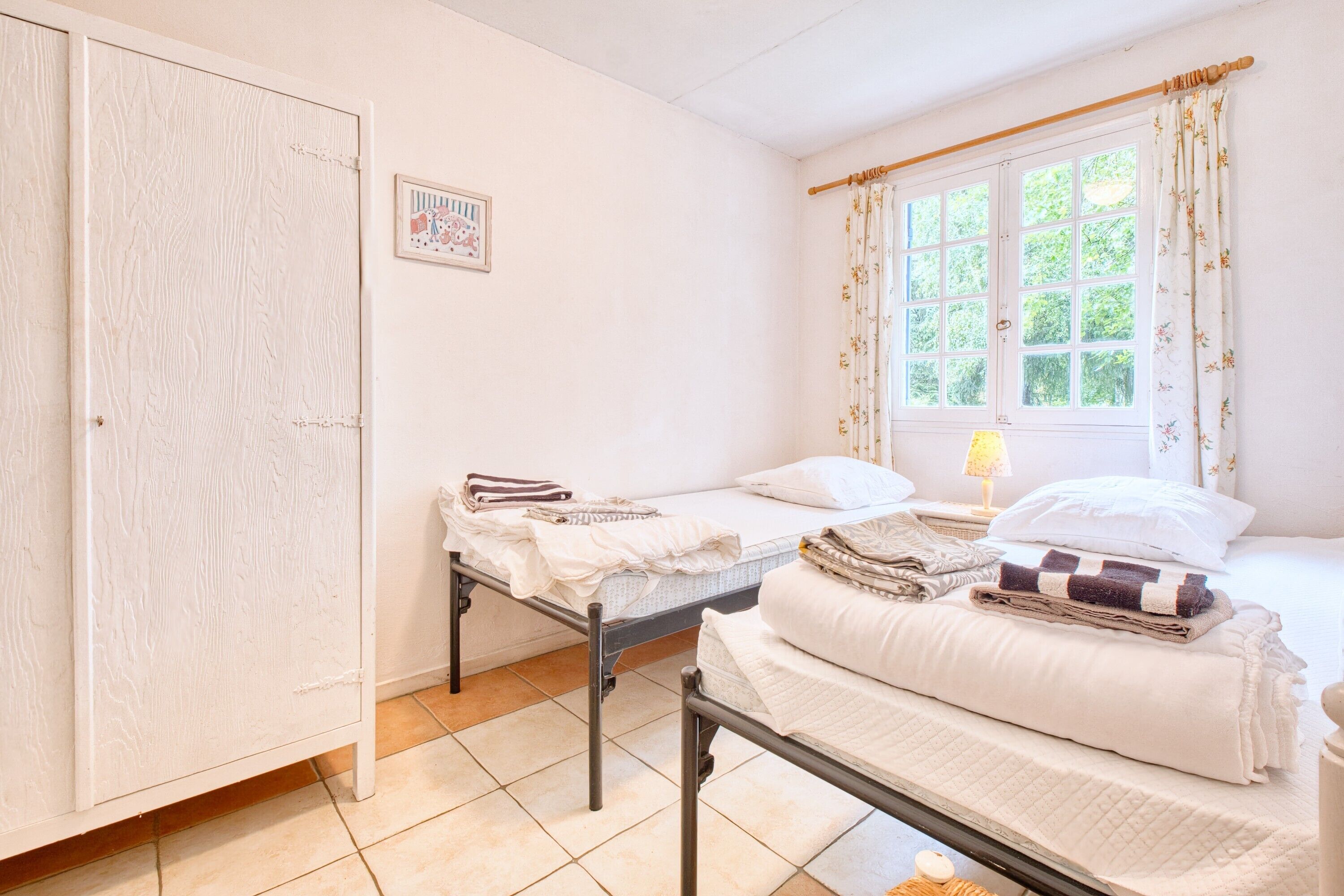 A bedroom with two beds, a wardrobe, a window with curtains, and a bedside lamp.