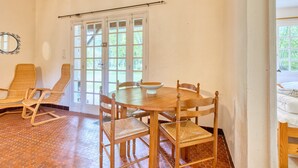 Un espace repas comprenant une table ronde en bois, six chaises en osier et un sol carrelé de forme hexagonale.