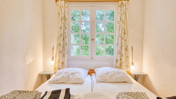 Une chambre avec deux lits, une fenêtre avec des rideaux, des lampes de chevet et une vue sur les arbres.