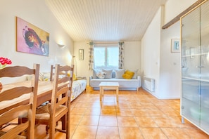 A room with a wooden dining table, a sofa with cushions, a window with curtains, and a glass cabinet. - Gîte Le Pont - Domaine l'Étang des Mirandes with Shared Pool (Varaignes)