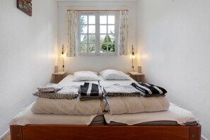 A neatly made bed with pillows and folded blankets, a window with curtains, and bedside lamps. - Gîte Le Lavoir - Domaine l'Étang des Mirandes with Shared Pool (Varaignes)