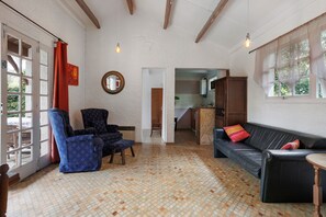 A spacious living area with a patterned floor, a black leather sofa, a blue armchair, and a wooden ceiling. - Gîte Le Lavoir - Domaine l'Étang des Mirandes with Shared Pool (Varaignes)