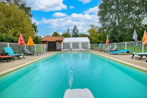 A swimming pool with lounge chairs and umbrellas, surrounded by a fence and trees. - Gîte Le Lavoir - Domaine l'Étang des Mirandes with Shared Pool (Varaignes)