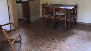 A dining area with a table and chairs, a kitchen in the background, and a window with curtains. - Gîte Le Lavoir - Domaine l'Étang des Mirandes with Shared Pool (Varaignes)