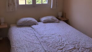 A bedroom with a bed, two bedside tables, a window with curtains, and a view of greenery outside. - Gîte Le Lavoir - Domaine l'Étang des Mirandes with Shared Pool (Varaignes)